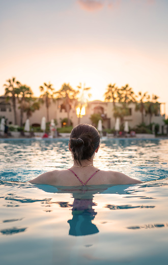 Woman enjoying the sunset in a tropical swimming pool overlooking the sea in an unrecognizable tourist resort