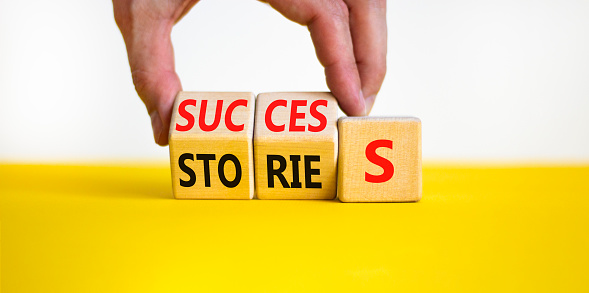 Success stories symbol. Businessman turns wooden cubes and changes the word stories to success. Beautiful yellow table, white background, copy space. Business success stories story concept.