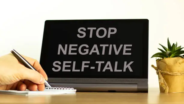 Stop negative self-talk symbol. Concept words Stop negative self-talk on the black tablet. Businessman hand with pen. Psychological and stop negative self-talk concept. Copy space.