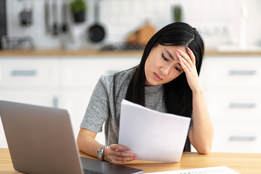 Sad depressed woman owner of small business holding documents, looks through sales dynamics or taxes and is upset. Loan, debt, bunkruptcy. Young female student received bad notification letter