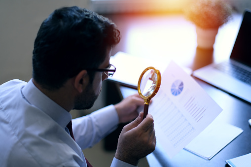 Focused businessman is reading through  magnifying glass document
