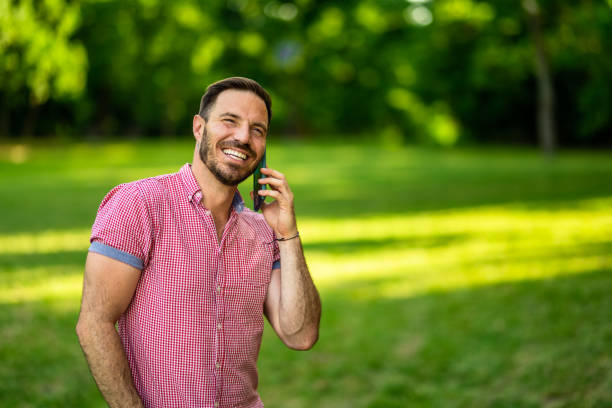 Cheerful man standing in nature and talking on cellphone. Copy space.