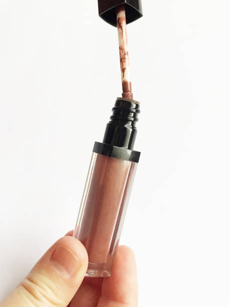 Female hand holding lip gloss brush on the white background
