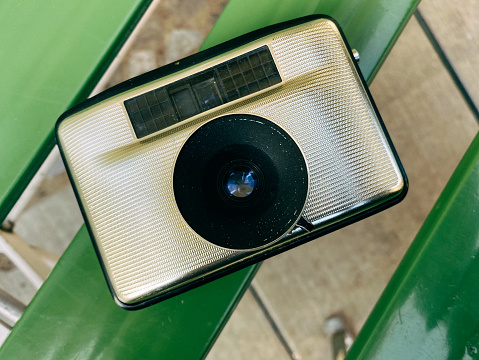 Close-up of a small old golden analog camera. It lies on a green garden chair and waits for its use.