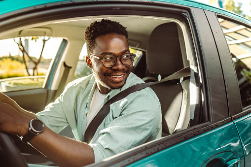 Feliz conductor afroamericano que conduce un automóvil y mira a través de la ventana del automóvil photo