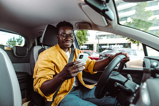 African-American man driving a car and looking at the smart phone