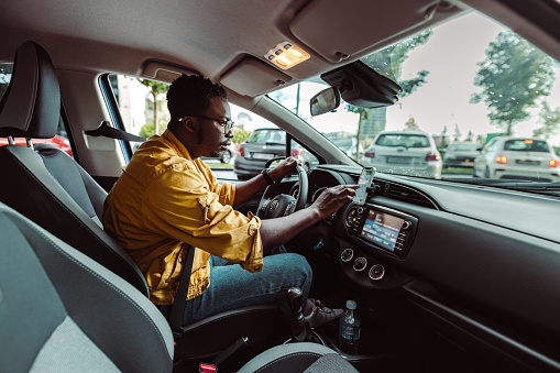 African-American man driving a care and using smart phone