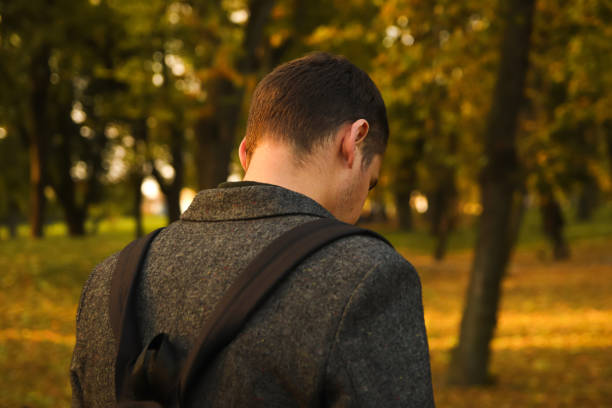 istock Defocus young man holding phone. Man using smart phone in autumn park. Typing text message or reading social media at mobile phone. Fall background. Cell phone. Back view. Rear. Backpack. Out of focus 1407924208
