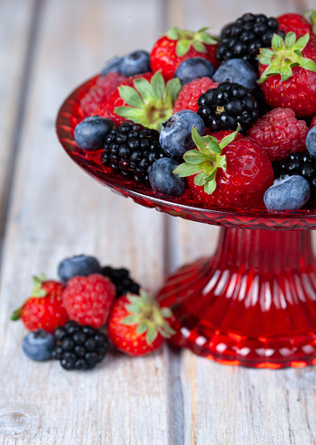 Assorted berries in a plate on white rustic wooden table