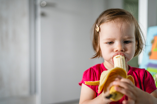 one small caucasian girl little toddler child eating banana at home copy space