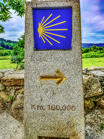 monolith stone landmark of the last 100 km on the Camino de Santiago and a beautiful landscape in the background