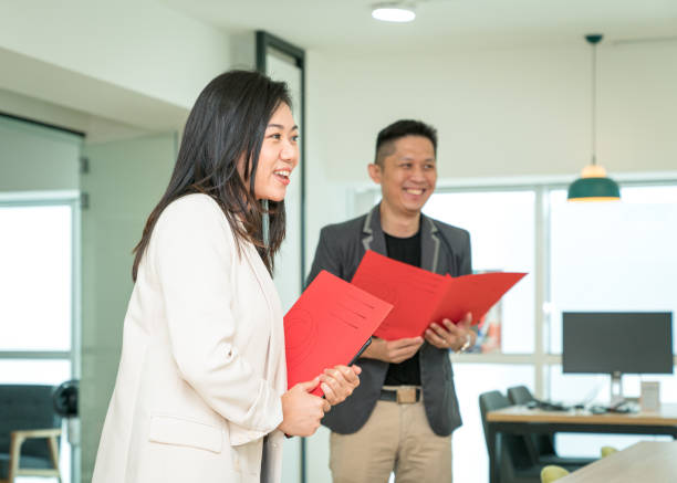 Businesswoman manager holding a file while talking and smiling, side view. Businesswoman manager holding a file while talking and smiling, side view. Office training or giving briefing concept. presentation folder stock pictures, royalty-free photos & images