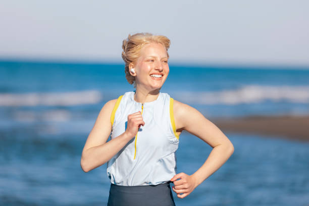 A fitness woman running by the ocean or sea beach with copy space. Running woman jogging on beach listening to music in earphones. Fitness and heath care concept.