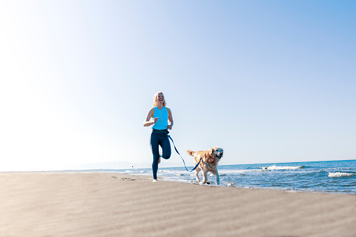 A young woman is active on summer vacation, running on the beach with her companion, a large purebred dog, keeping her company