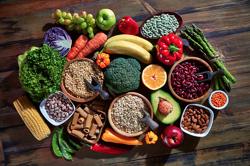 Vegan food themes. Table top view of fresh vegetables and legumes on rustic wooden table. Food is rich of fiber ideal for dieting and healthy eating. Includes corn, avocado, broccoli, orange fruit, grapes, bell pepper, lettuce, banana, apple  almonds and wholegrain pasta, bread.