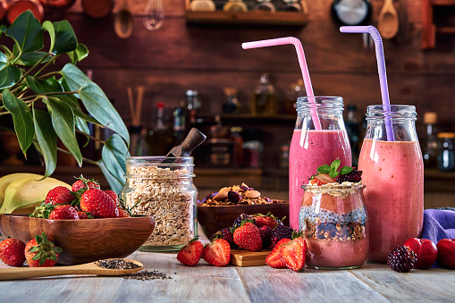 Vegan food themes. Set of three banana blackberry and strawberry smoothies with cereal in bottles with straws on table in a rustic kitchen.