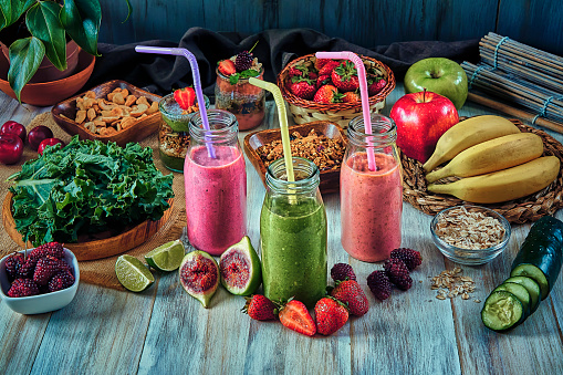 Vegan food themes. Healthy food: Set of four banana blackberry, strawberry and green vegetables detox smoothies in bottles with straws in a rustic kitchen