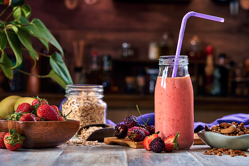 Healthy food: Banana and strawberry smoothie with cereal in bottle with straws on a rustic table.