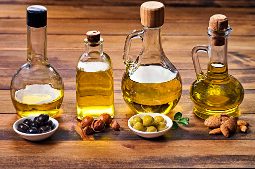 Assorted healthy vegetable oil bottle collection on wooden table in a old fashioned kitchen with low key illumination: Olive oil, hazelnut oil, almond oil, coconut oil and sesame oil