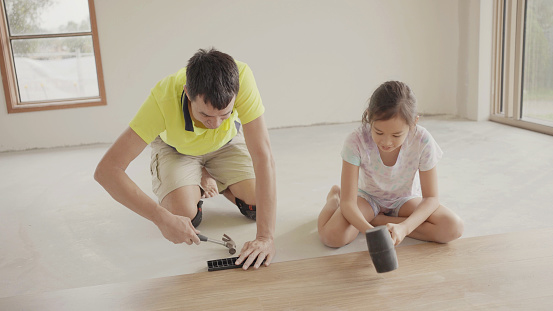 Father teaching daughters to install timber laminated wooden floor, home improvement, house renovation project, homeschooling concept