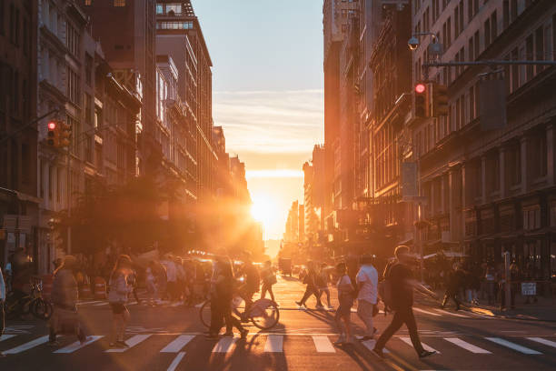 Busy intersection with crowds of people walking across the intersection at 23rd Street and 5th Avenue in New York City with sunset light shining in background stock photo