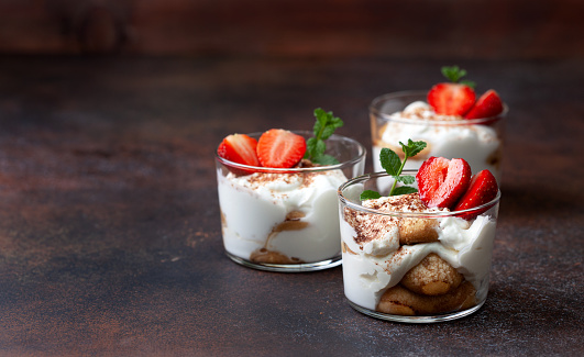 tiramisu with strawberries in glasses on a brown background
