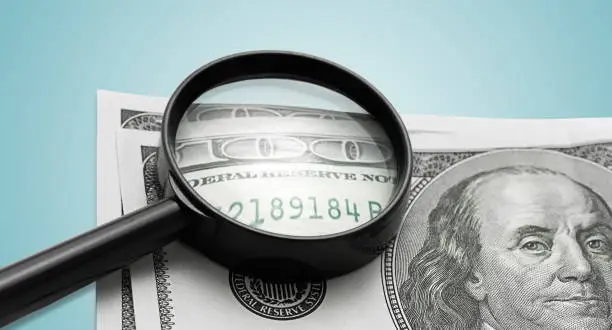 Photo of Magnifying glass and one hundred dollars on a blue background