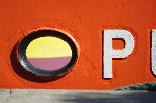 Hawse hole and P letter in the broadside of a orange ship in the port of Barcelona.