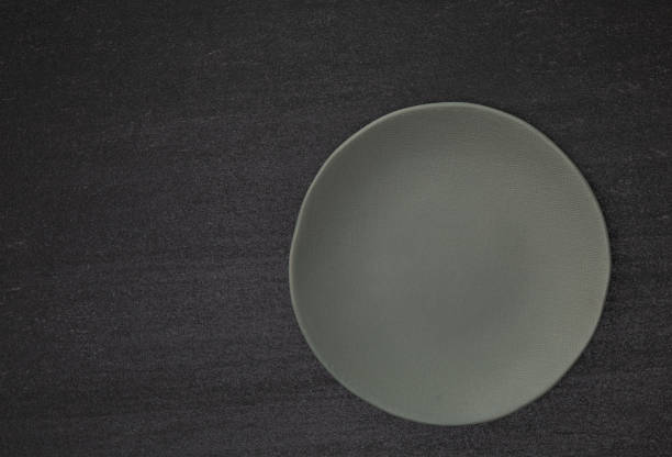 Empty blank gray ceramic round plate or dish on black stone blackground with copy space, Top view of traditional handcrafted kitchenware concept