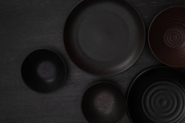 istock Group of empty blank black ceramic round bowls and plates on black stone blackground, Top view of traditional handcrafted kitchenware concept 1407955067