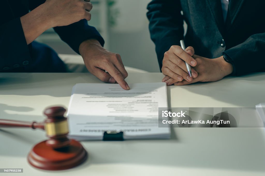 Male businessman and lawyer consulting with the client team on law, discussing and signing office contract with judge's scale and hammer on legal services concept table. Legislation Stock Photo