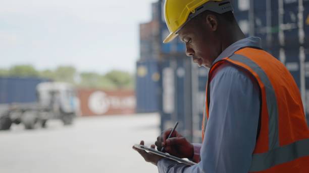 istock African American engineer or foreman or male worker working, hold tablet checking at control loading container system or harbor device maintenance system. Supervisor use tablet monitoring unloading cargo real time. 1407955340