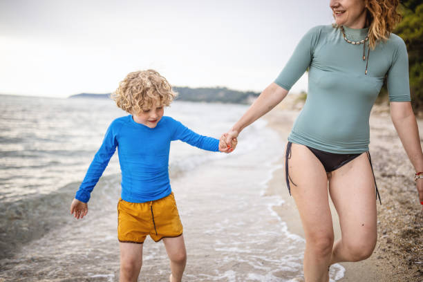 Photo of surfer boy and his mum enjoys in walk by the sea