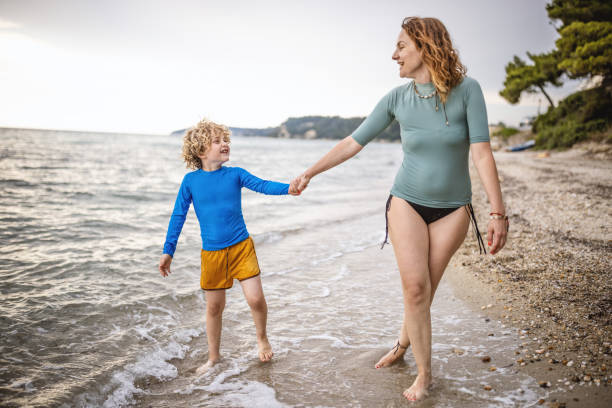 Photo of surfer boy and his mum enjoys in walk by the sea, before he gets the surfing class.