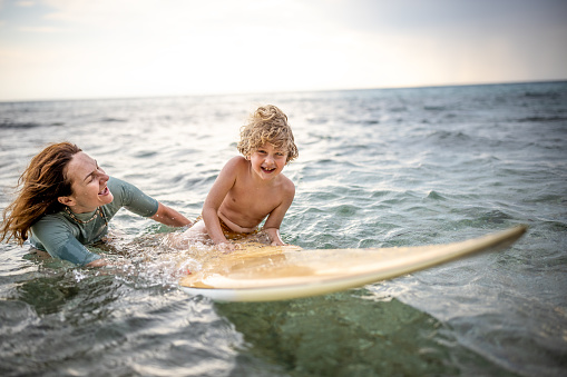 Photo of little surfer learn to ride on surfboard with help of his mother