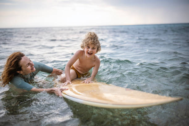 istock Little surfer learn to ride on surfboard with mother 1407957647