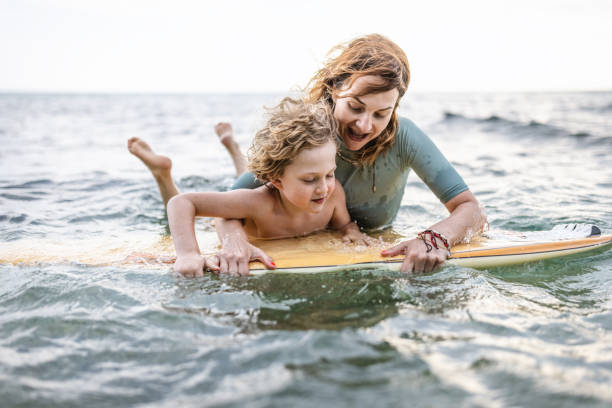istock Little surfer learn to ride on surfboard with mother 1407958420