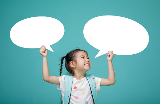 Smiling happy Asian little girl with blank speech bubbles, empty space in studio shot isolated on colorful blue background, Educational concept for school