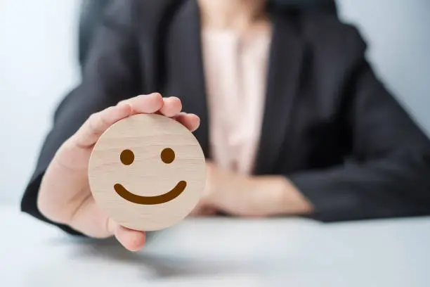 Photo of hand holding smile face block. Customer choose Emoticon for user reviews. Service rating, ranking, customer review, satisfaction, mood, mental health and feedback concept
