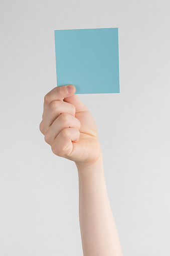 child hand holding a square blue blank reminder or paper notes above a white and gray background, copy space