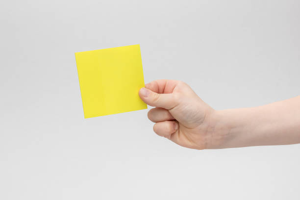 mano del bambino che tiene un promemoria vuoto giallo quadrato o note cartacee sopra uno sfondo bianco e grigio, spazio di copia - luggage hold foto e immagini stock