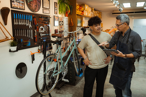 Asian man talking to the senior man owning the bike shop and inquiring about the features of the bike.