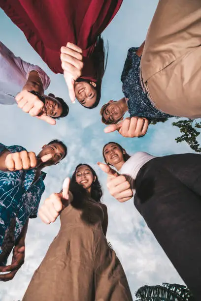 Photo of Six young friends gather together and give a thumbs up. Shot from the ground looking up. Successful teamwork concept.