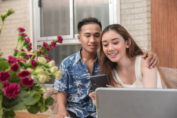 A young woman checks her social media feed with her boyfriend. A happy Gen Z couple on the couch. A young woman checks her social media feed with her boyfriend. A happy Gen Z couple on the couch. happy malay couple stock pictures, royalty-free photos & images
