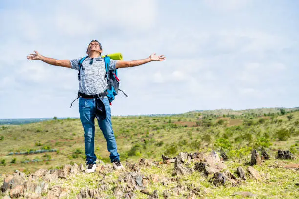 Photo of Middle aged man feeling or admiring natures fresh air by stretching arms during hiking at hill top - concept of refreshment, active healthy lifestyle and holidays