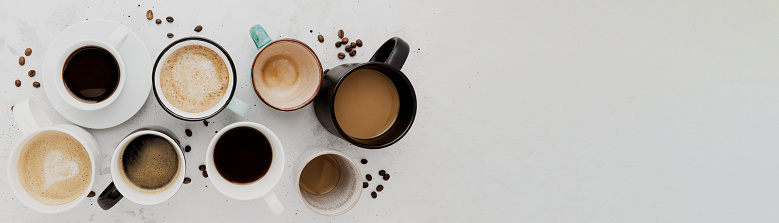 Top view on flat lay with many different full and empty coffee cups composition on gray white concrete background. Variety of tea mug collection layout. Dried coffee beans. Espresso, latte, americano