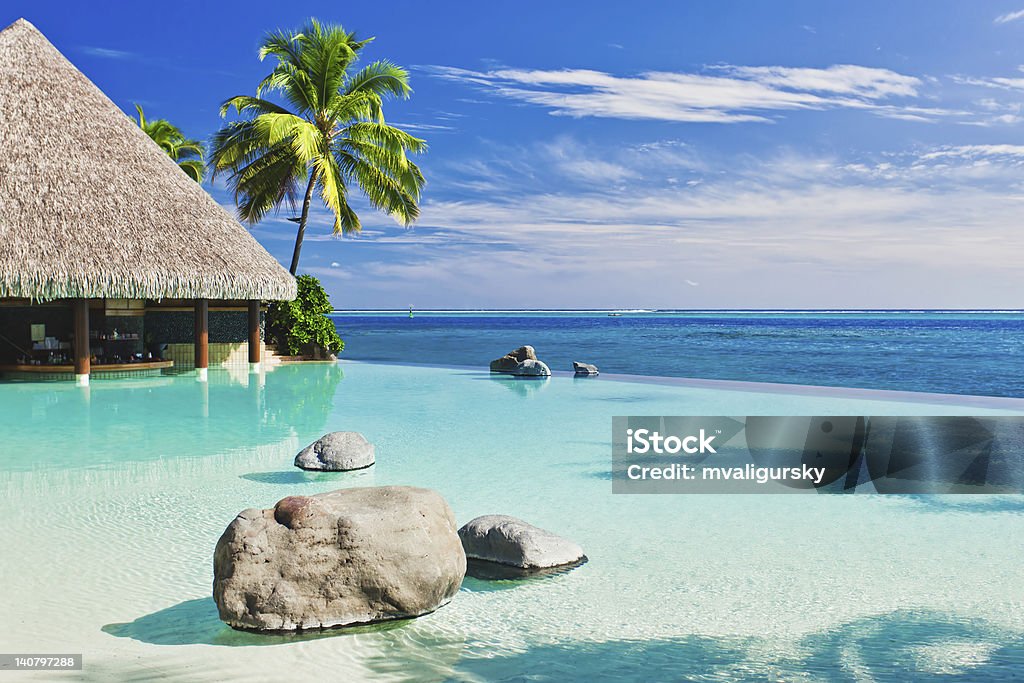 An infinity pool with artificial beach and blue ocean Infinity pool with artificial beach and tropical ocean Bay of Water Stock Photo