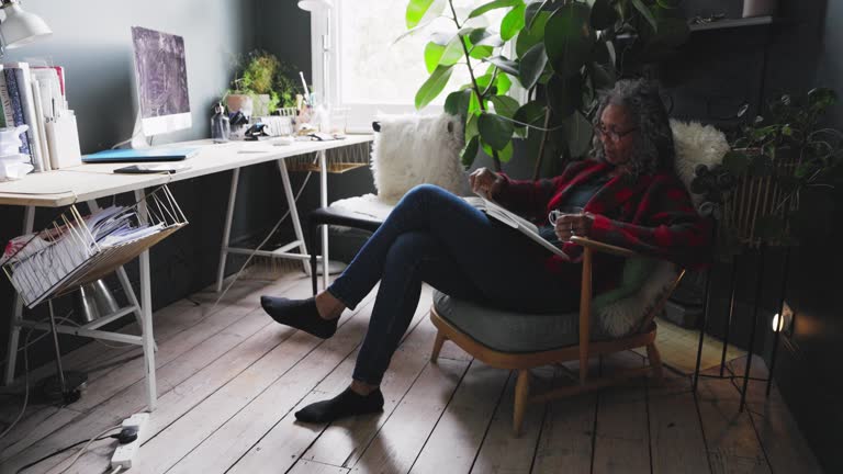 Senior woman reading book and drinking tea in home office