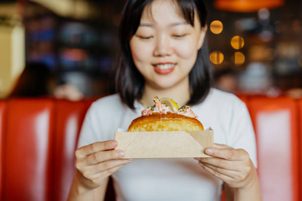 une femme asiatique tenant un rouleau de homard dans un récipient en papier - freedom sandwich bread food photos et images de collection