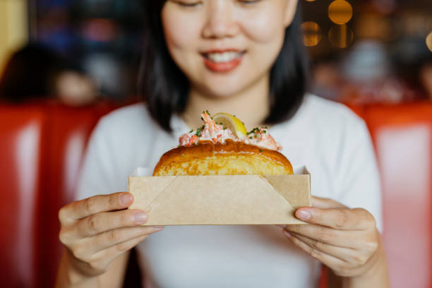 eine asiatische frau, die hummerrolle in einem papierbehälter hält - freedom sandwich bread food stock-fotos und bilder